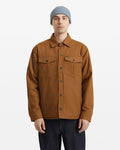 A person wearing a light blue knit beanie, dark jeans, and the Volcom Men's Westmead Jacket—a brown button-up with chest pockets—stands facing forward against a plain white background.