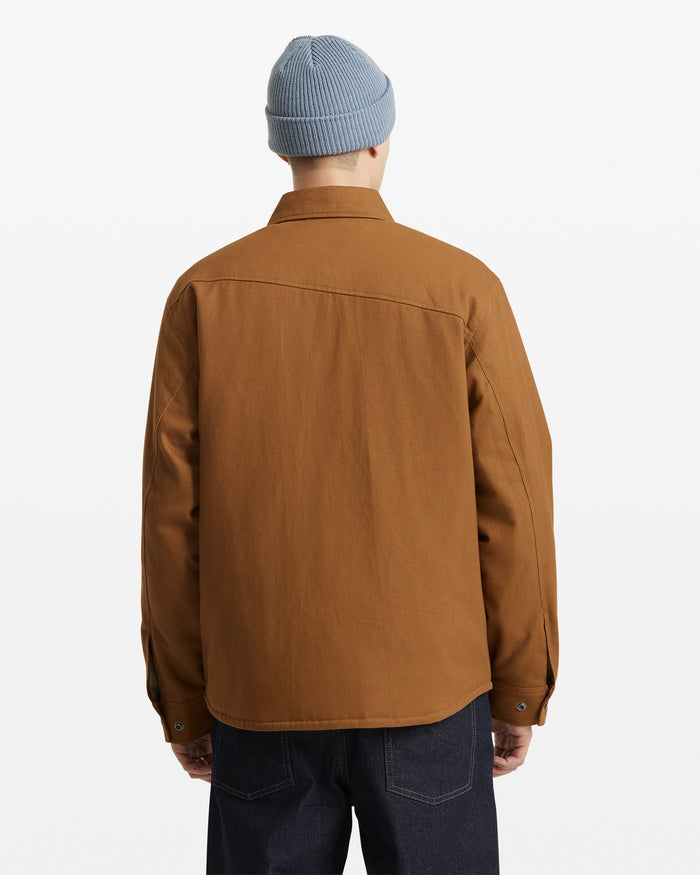 A person is shown from the back against a plain white background, wearing dark jeans, a light blue knit beanie, and the Volcom Men's Westmead Jacket in brown.