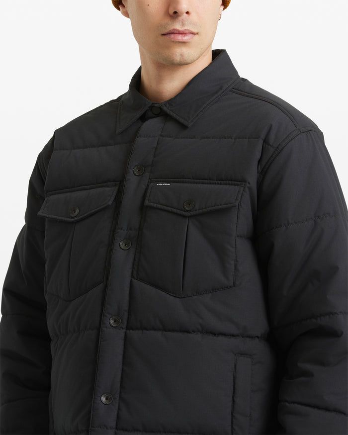 A man wearing the Volcom Men's Westmead Quilted Jacket, featuring a buttoned front and two chest pockets, is shown from the chest up against a plain white background.