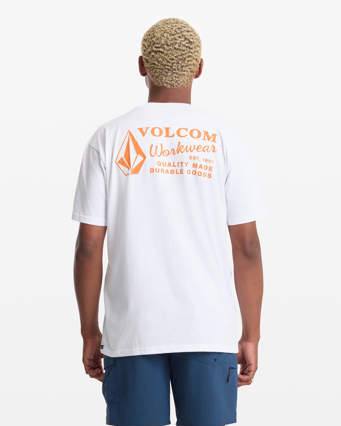 A man with short, curly blond hair wears a white Volcom Men's Workwear Short Sleeve Tee with an orange logo and text on the back, paired with blue shorts, standing against a plain white background.