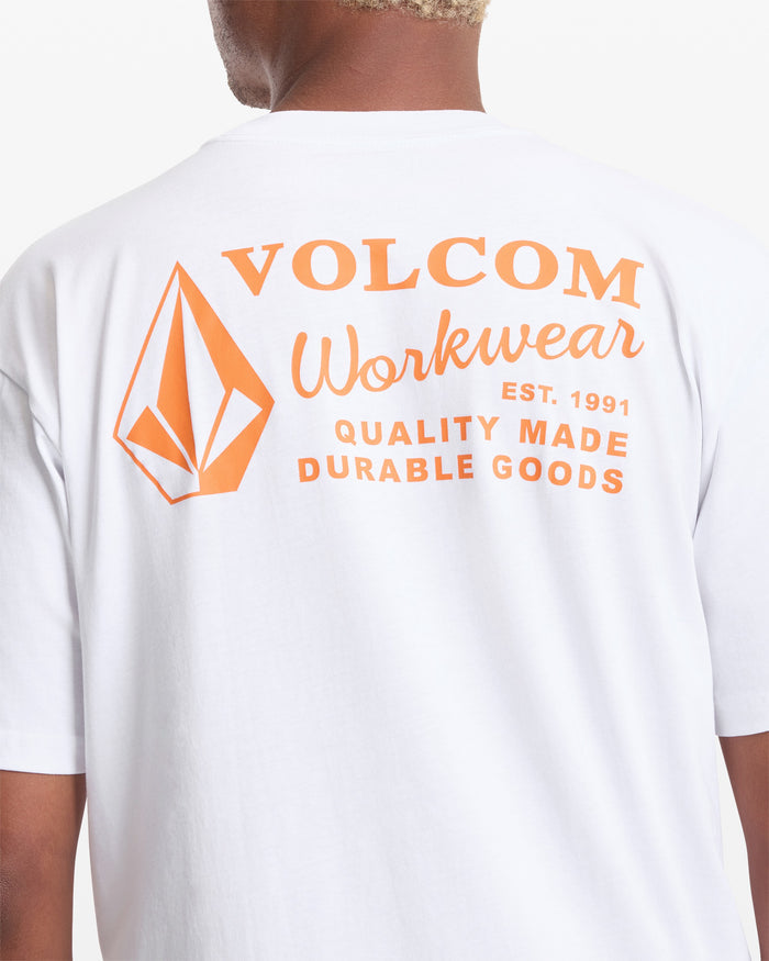 A person wears the Men's Workwear Short Sleeve Tee by Volcom, a white organic cotton tee with an orange "VOLCOM Workwear Est. 1991" and geometric logo on the back, designed for comfort and style.