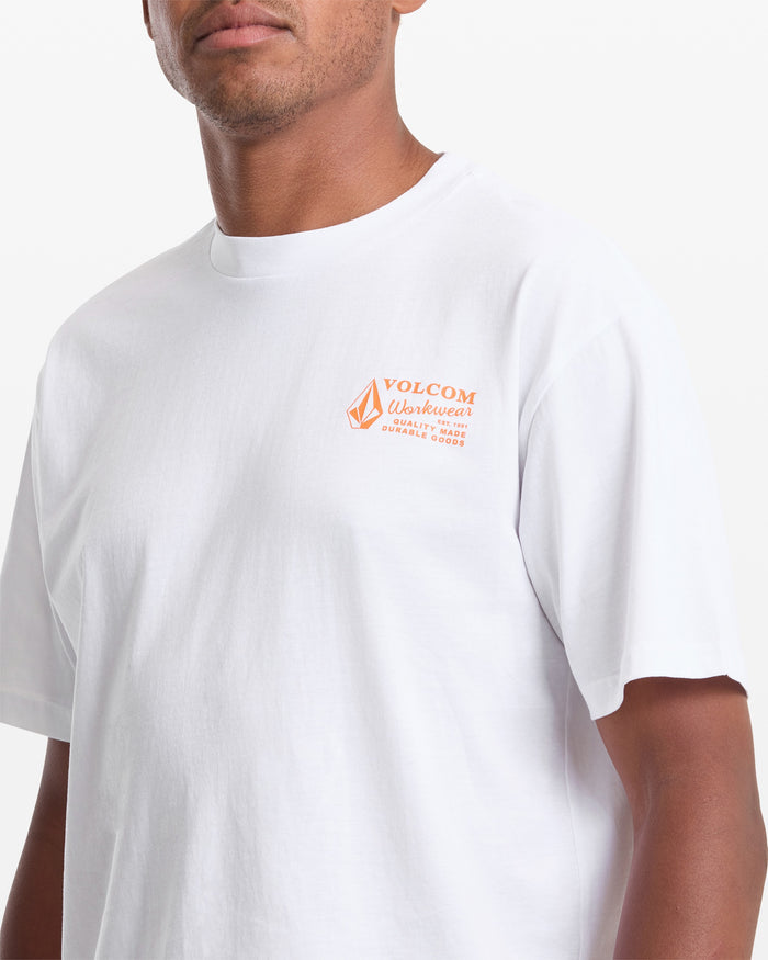 A man wears a Volcom Men's Workwear Short Sleeve Tee in white, featuring an orange Durable Goods logo on the left chest, standing against a white background.