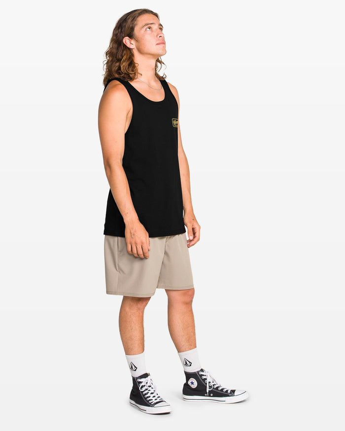 A person with long hair stands against a plain background, wearing a black Volcom Men's Wrecking Tank (100% cotton), beige shorts, white socks, and black high-top sneakers, gazing slightly upward to the right.