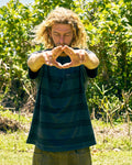 A person with curly blond hair stands outdoors before green foliage, wearing the Volcom Men's Yewster Crew Short Sleeve Tee. They extend their arms forward, forming a triangle with their hands as they look down.