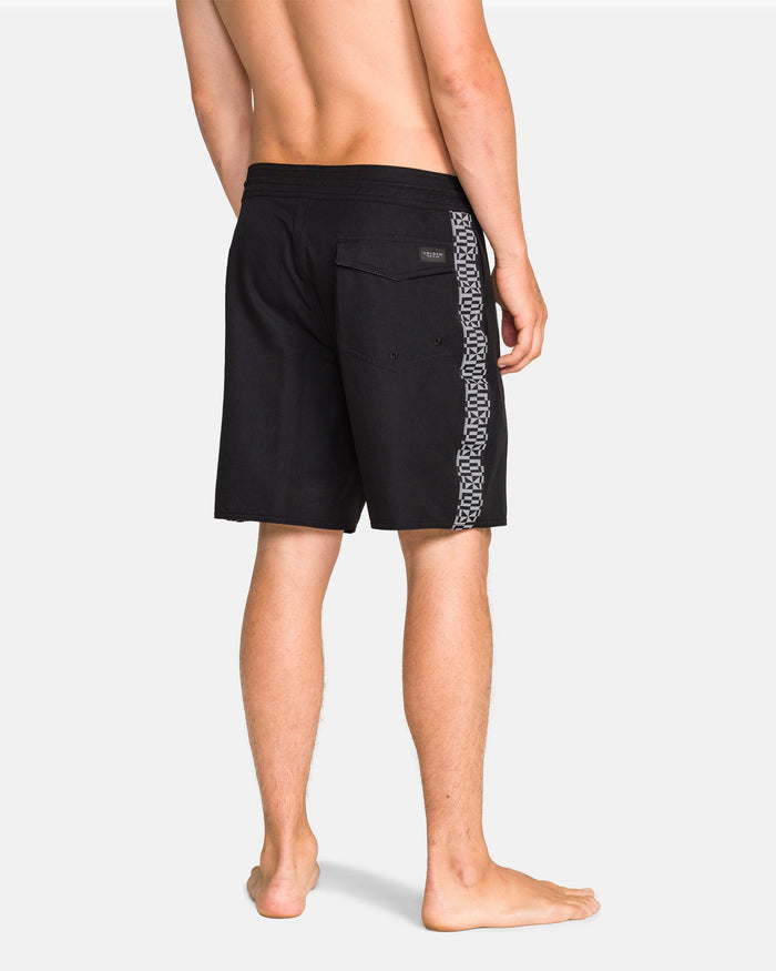 A barefoot man faces away wearing Volcom Men's Yewster Loose Stoney black boardshorts with a patterned stripe, showcasing the back pocket and label. Made with Stone Hemp Stretch for lasting comfort and durability.