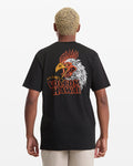 A person with short blond hair is seen from behind wearing the Volcom Men's Yewster Rooster Short Sleeve Tee, a black T-shirt with a colorful rooster graphic and "VOLCOM HAWAII" text on the back.