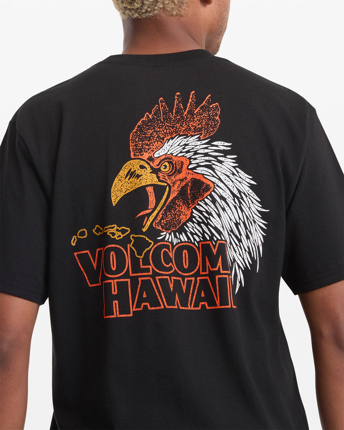 A man wears the Volcom Men's Yewster Rooster Short Sleeve Tee, which has a large, colorful rooster head graphic above "VOLCOM HAWAII" and an outline of the Hawaiian islands on the back.