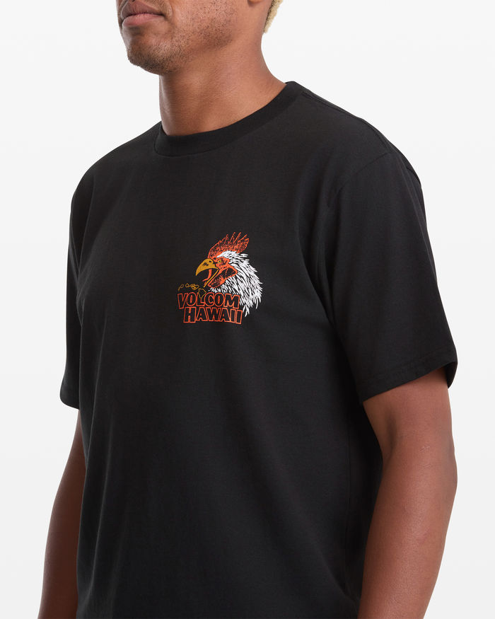 A man wears the Volcom Men's Yewster Rooster Short Sleeve Tee in black, featuring a colorful rooster graphic and "Volcom Hawaii" text on the left chest.