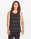 A young man with long brown hair stands and smiles at the camera against a plain white background, wearing a modern fit Men's Yewster Tank by Volcom in black and gray jacquard stripes paired with black shorts.