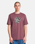 A man stands against a white background wearing the Volcom Men's Yoink Short Sleeve Tee, a classic fit maroon crew neck with a bold black and white geometric compass and diamond logo on the chest. Made from 100% cotton for comfort.