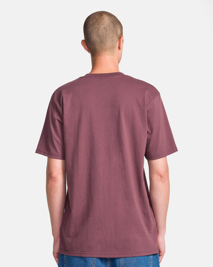 A person with short hair stands with their back to the camera, wearing a plain maroon Men's Yoink Short Sleeve Tee by Volcom and blue jeans against a light background.