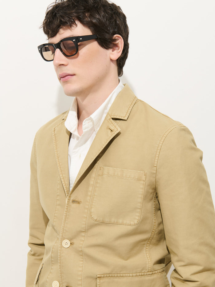 A man with short dark hair wears black sunglasses, a white shirt, and the Mill Blazer In Vintage Twill by Alex Mill with patch pockets, standing against a plain white background.