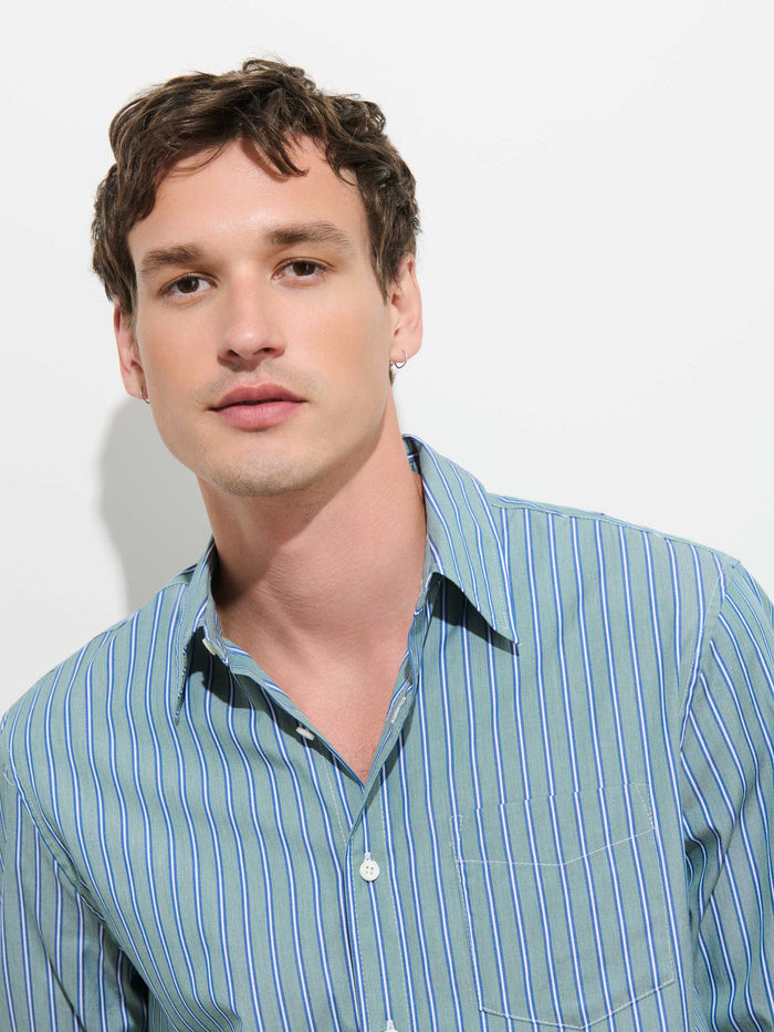 A young man with short brown hair wearing the Mill Dress Shirt In End-on-End Stripe, a perfect 100% cotton blue and green striped button-down shirt, poses against a plain white background.