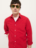 Wearing the Mill Shirt In Cotton Poplin, a bright red 100% cotton men's button-down, a white undershirt, and green-tinted sunglasses, a person stands against a plain white background with one arm behind their back.