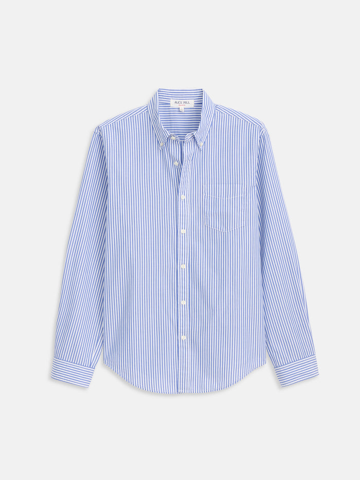 The Mill Shirt In Stripe Portuguese Poplin is a long-sleeved, button-up shirt with blue and white vertical stripes, a front chest pocket, and made from crisp Portuguese cotton. Displayed against a plain white background.