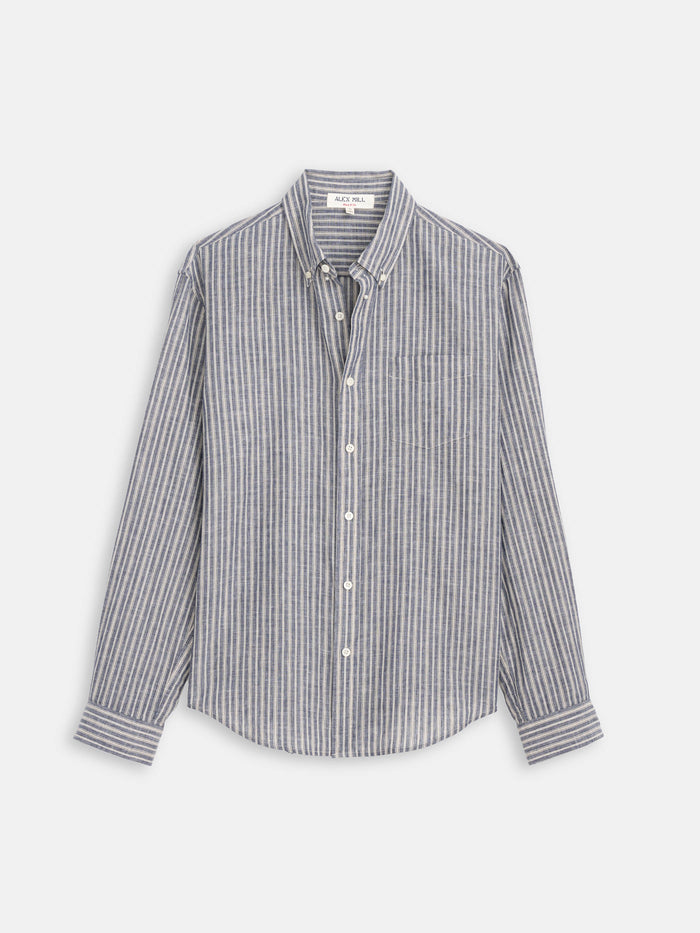 The Mill Striped Shirt In Chambray is a long-sleeve, button-down cotton-linen shirt with a collar and vertical blue, white, and grey stripes, shown against a plain white background—a perfect choice from Alex Mill.
