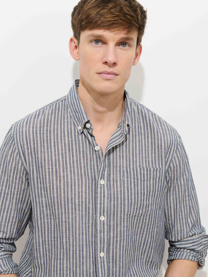 A young man with short brown hair wears the Mill Striped Shirt in Chambray, standing against a plain white background and looking directly at the camera with a neutral expression.