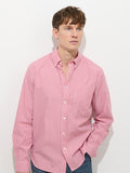 A young man stands against a white background, wearing the Mill Striped Shirt in cotton poplin—red and white stripes—and blue jeans, with one hand in his pocket and a neutral expression.