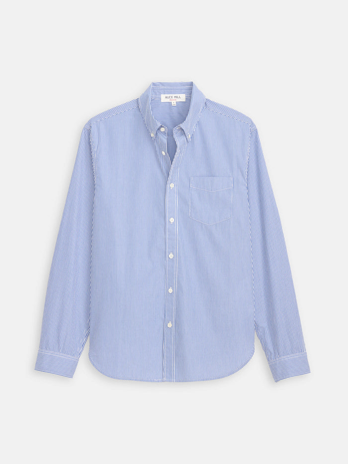 The Mill Striped Shirt in Cotton Poplin features light blue and white vertical stripes, long sleeves, a front chest pocket, and is crafted from 100% cotton. Shown laid flat on a white background.