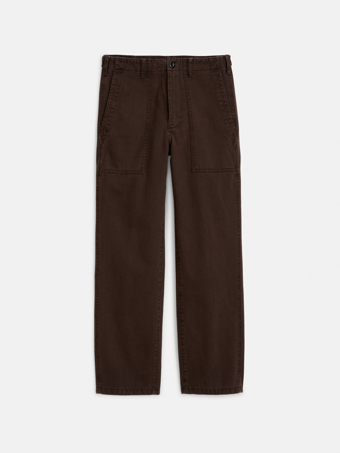 The Neil Pant In Herringbone features a brown straight-leg silhouette, button closure, front patch pockets, and visible stitching detail. Crafted from herringbone cotton, it is shown laid flat on a white background.