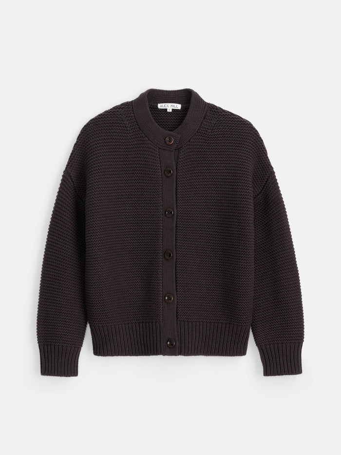 Introducing the Nico Cardigan in Cotton—a timeless women’s designer sweater in dark brown, featuring long sleeves, a textured knit pattern, ribbed cuffs and hem, corozo button closure, and a classic round neckline. Perfect for effortless layering.