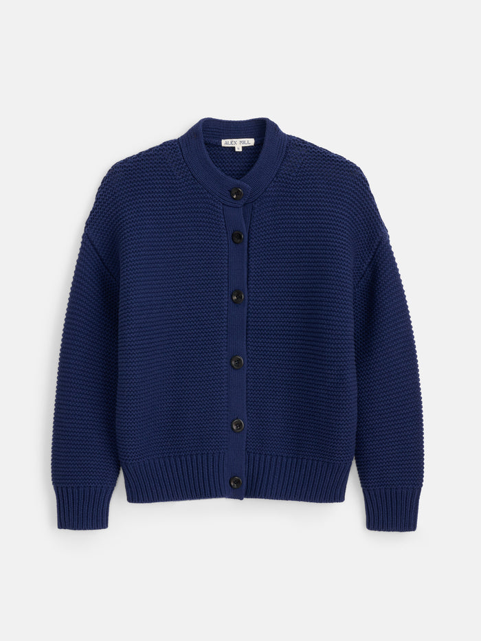 The Nico Cardigan in Cotton is a navy blue, long-sleeve women’s sweater made from 100% cotton knit, featuring black Corozo buttons down the front and ribbed cuffs, collar, and hem. It is shown laid flat against a white background.