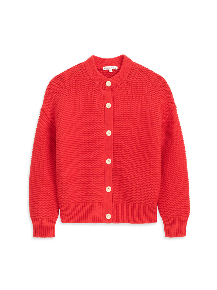 The Nico Cardigan In Cotton is a bright red chunky knit with a textured pattern, white corozo front buttons, a round neckline, long sleeves, and ribbed cuffs and hem.