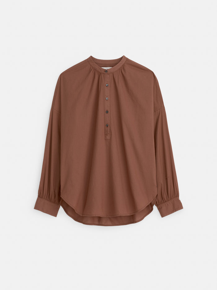The Nina Popover in Cotton Voile is a loose-fit, long-sleeve women's designer shirt in brown, made from 100% cotton voile with a round neckline, partial button placket, gathered cuffs, and a curved hem, shown on a plain white background.