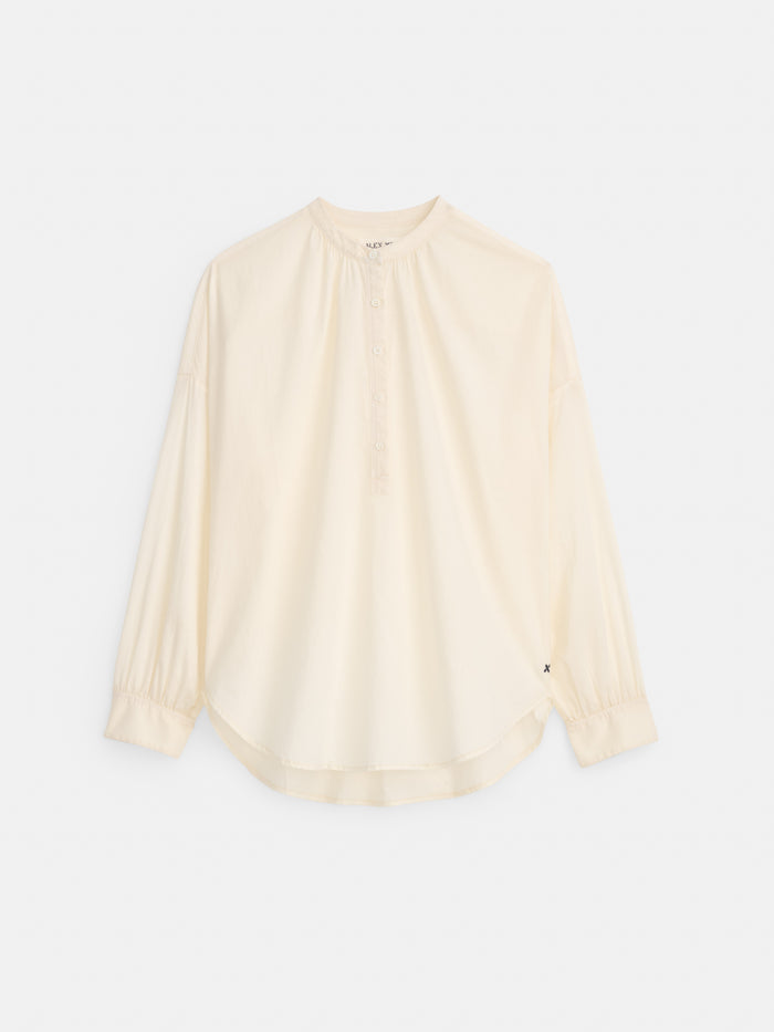 The Nina Popover in Cotton Voile is a loose-fitting, long-sleeve oversized off-white blouse made from 100% cotton voile, with a round collar, partial button placket, and subtly gathered cuffs, shown on a plain white background.