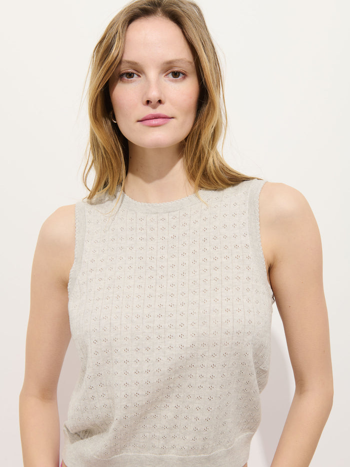 A woman with light brown hair models the Odette Sweater Tank in cotton cashmere—a sleeveless, light beige top with a subtle pattern and feminine fit. She faces the camera with a neutral expression against a plain white background.
