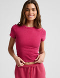 Woman wearing a red ribbed cropped t-shirt and red shorts against a plain background.