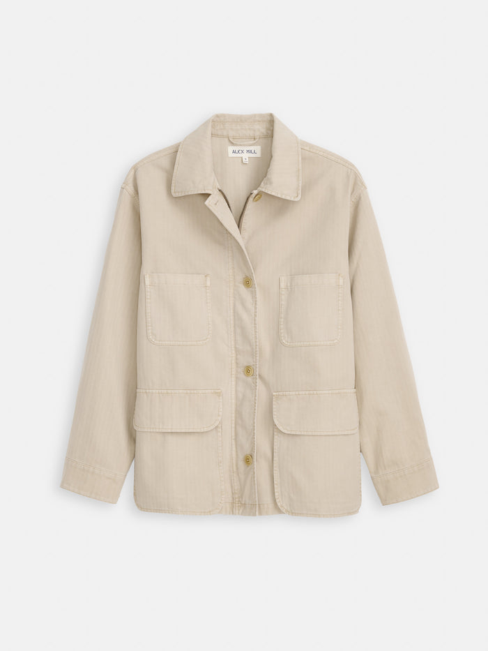 The Painter Jacket In Herringbone is a beige, long-sleeve cotton jacket with a collar, button-down front, oversized fit, and four large front pockets, shown flat on a white background.