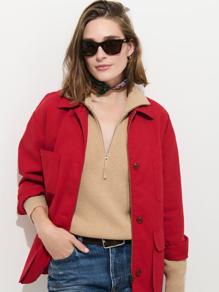 A woman wearing a tan sweater, blue jeans, sunglasses, and a colorful scarf stands against a white background. She has shoulder-length hair and has one hand in her pocket. She layers her outfit with the Painter Jacket In Herringbone for an oversized look.