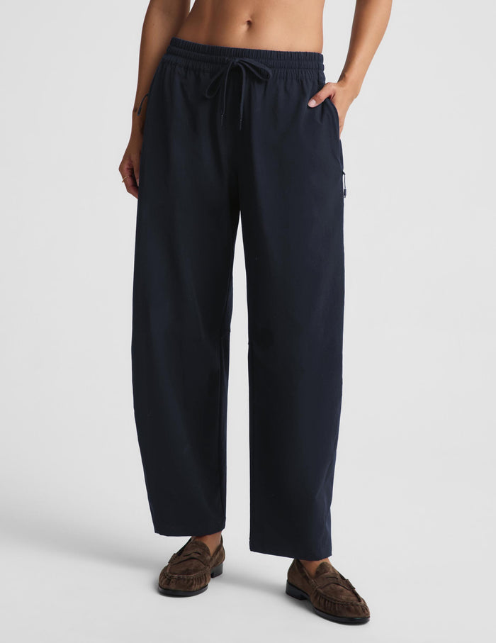 A person wearing loose dark navy drawstring pants with side pockets and brown mule loafers, photographed against a clean light gray studio background.