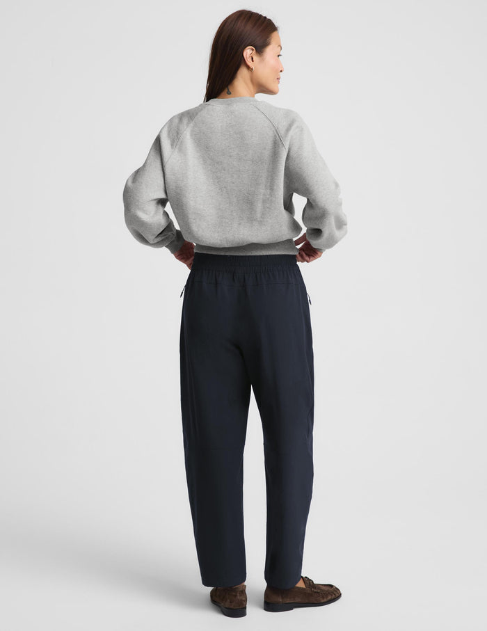 A woman modeling a light gray crewneck sweatshirt and dark navy wide-leg drawstring pants, paired with brown loafers, against a solid light gray studio background.