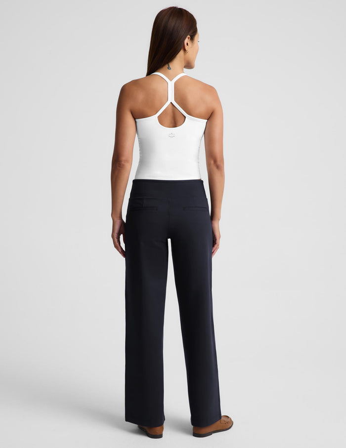 A woman shown from the back wearing a white racerback tank top with crisscross straps and dark navy wide-leg pants, photographed against a light gray studio background.