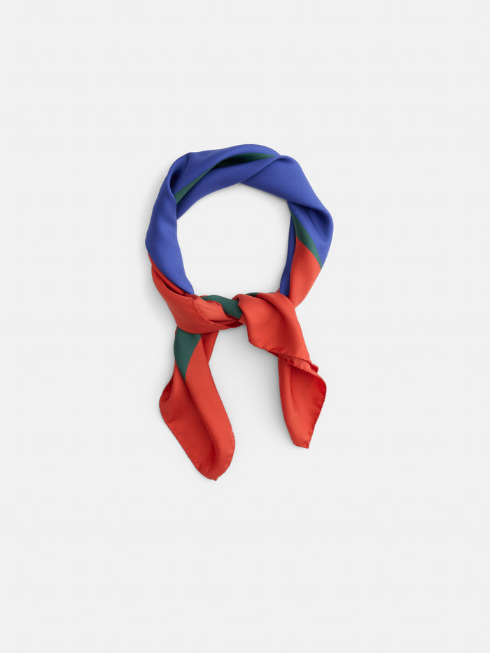 The Pop Art Silk Scarf, featuring striking blue, red, and green panels, is loosely knotted and displayed against a plain white background.