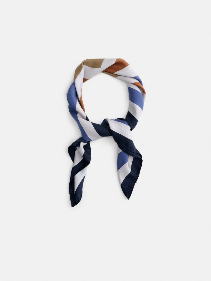 The Pop Art Silk Scarf, featuring diagonal stripes in navy, white, blue, brown, and rust, is tied in a loose knot against a plain white background.