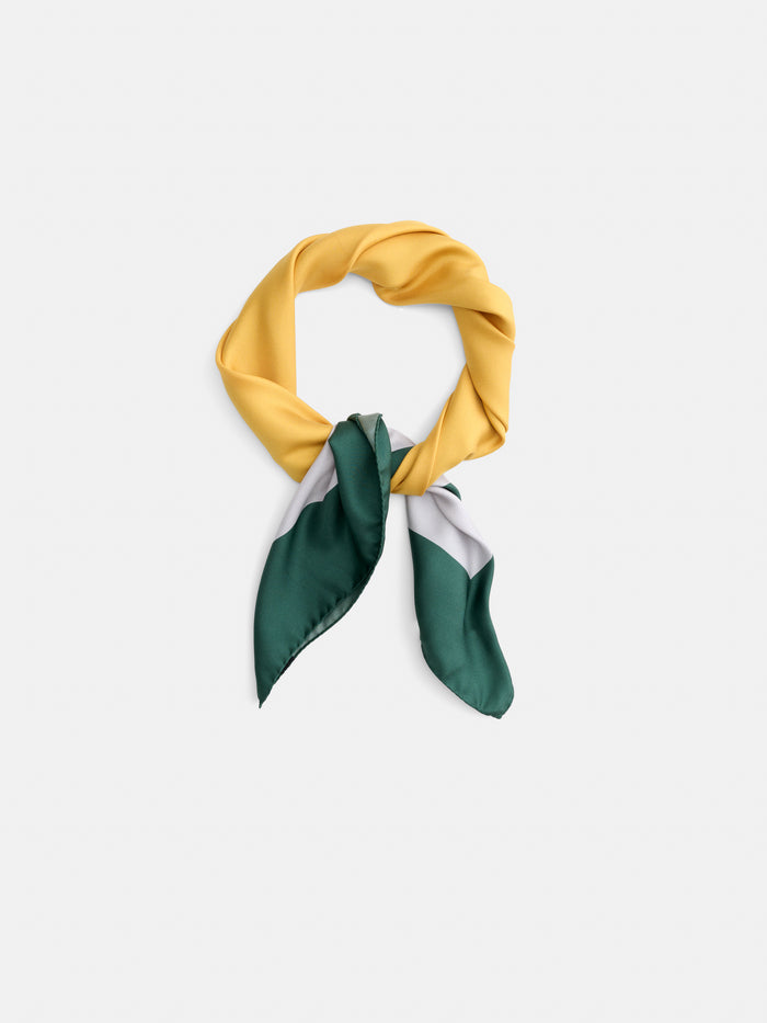 The Pop Art Silk Scarf, featuring a twisted yellow loop and pointed green, gray, and white ends, is laid flat on a white background.