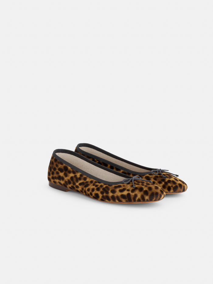 The Prince Street Ballet Flat in Calf Hair, handmade in Florence from luxurious Italian leather, showcases a chic leopard print with black trim and delicate bows at the toes, elegantly displayed against a plain white background.