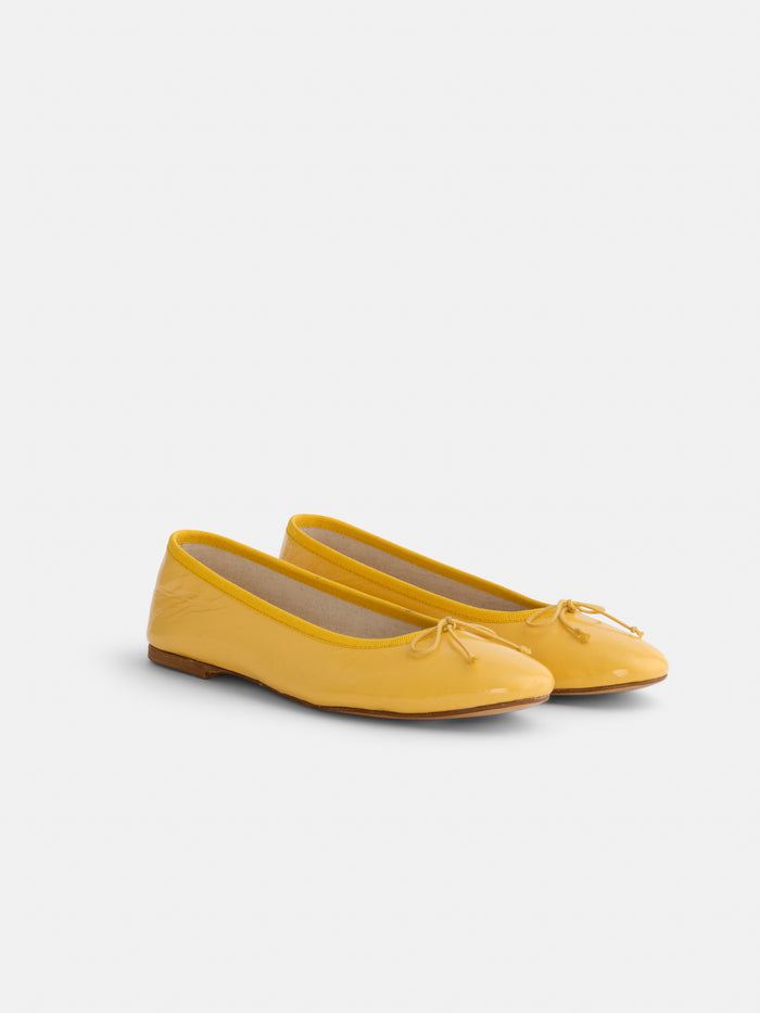 A pair of glossy yellow Prince Street Ballet Flats with small bows on the toes, handmade in Florence from Italian leather, is displayed on a plain white background.