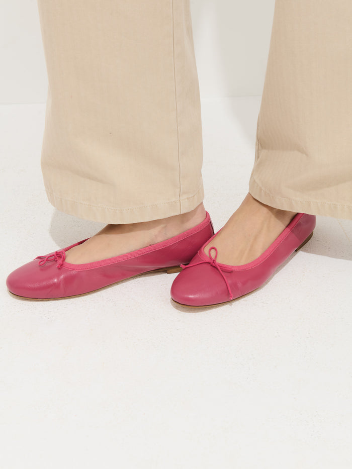 Someone stands on a white floor wearing beige wide-leg pants and bright pink Prince Street Ballet Flats, handmade in Florence and featuring small bows.