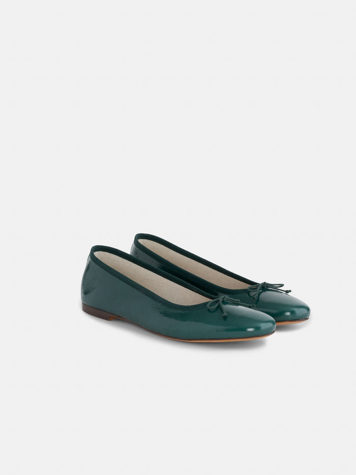 A pair of Prince Street Ballet Flats in patent leather, crafted in Italy in a dark green hue with delicate bows adorning the toes, displayed against a simple light background.