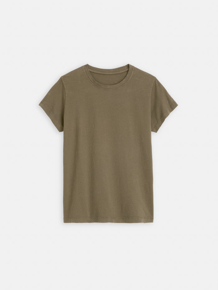 The Prospect Tee In Cotton Jersey is a women’s short-sleeve t-shirt in olive green, made from 100% cotton. Laid flat on a white background, it features a classic crew neckline and garment-dyed fabric for comfort and timeless style.