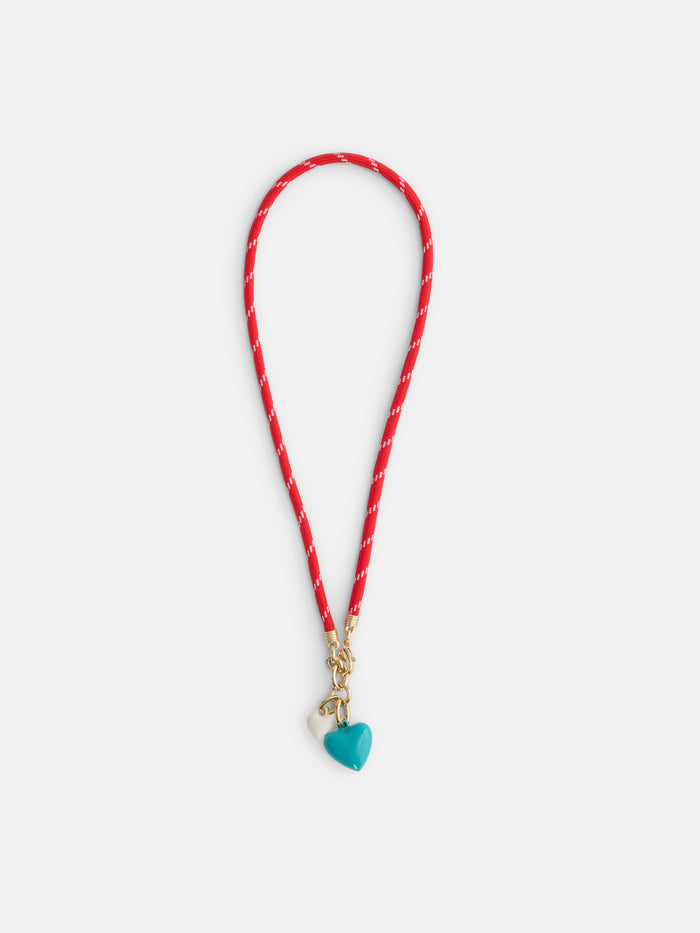 The Roxanne Assoulin Happy Cord Charm Necklace features a colorful cord with white accents, gold clasps, and two puffy heart pendants—one turquoise and one cream—dangling at the center.