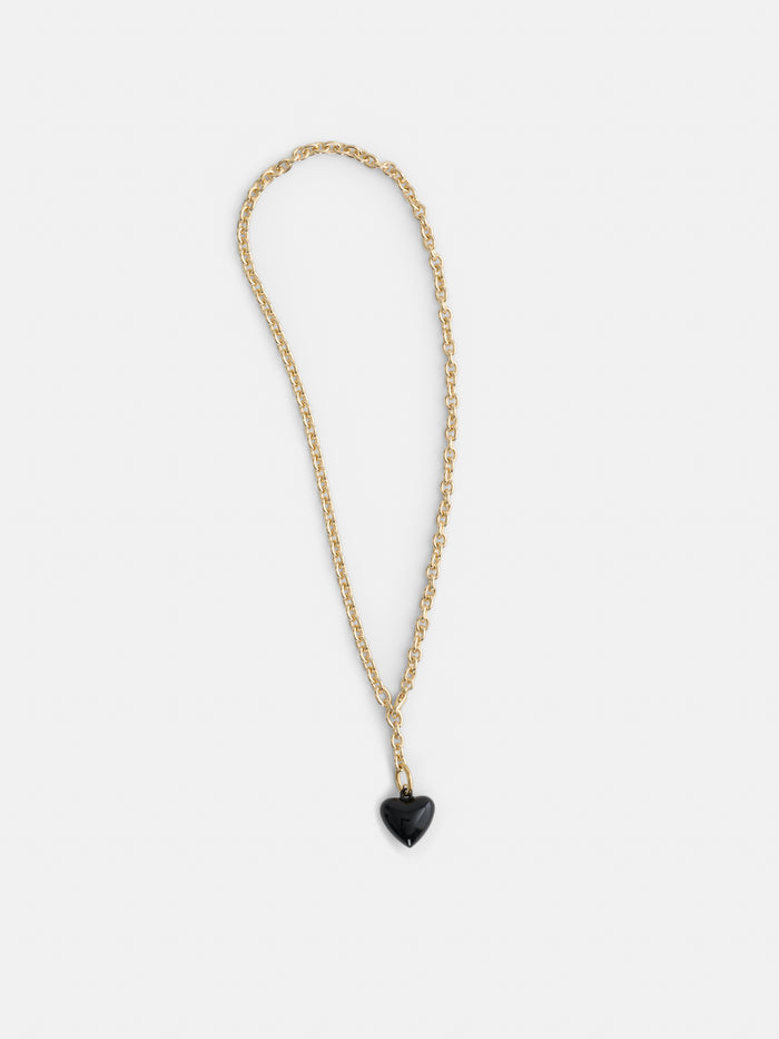 The Roxanne Assoulin Mini Puffy Heart Necklace features a gold puffy heart and a small black heart-shaped pendant on a brass cable chain, shown against a plain white background.