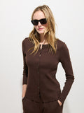 A woman wearing dark sunglasses and the Scout Cardigan in Cotton Rib in a brown, long-sleeve style stands against a white background, with her hands in her pockets and hair draped loosely around her shoulders.