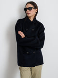 A person wearing sunglasses, light-colored pants, and the Sophia Coat In Wool—a dark double-face, double-breasted coat with hand-stitched seams—stands with arms loosely folded against a plain white background.