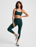 Woman wearing a green racerback sports bra and matching high waisted capri leggings against a plain studio background.
