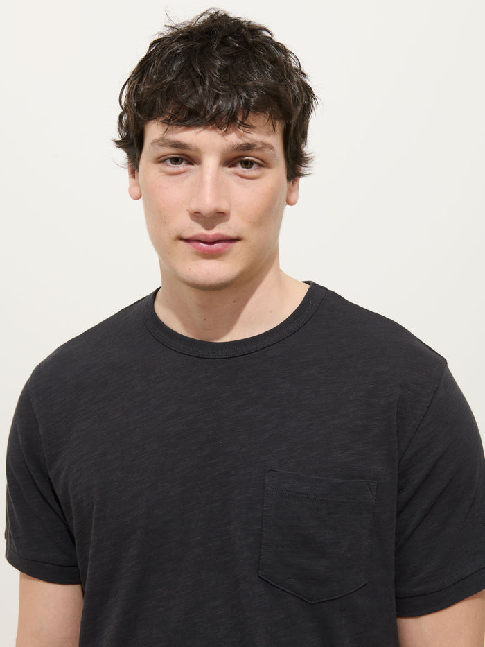 A young man with short, dark, wavy hair wears the Standard Slub Pocket Tee in black, standing against a plain white background and looking at the camera with a neutral expression.